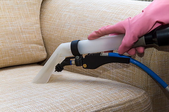 Person with pink glove cleaning sofa