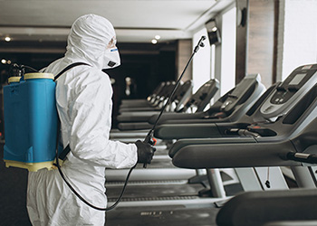 Man in full cleaning gear cleaning a gym 