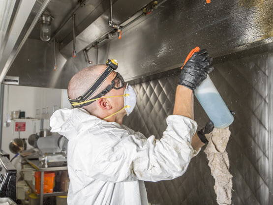 Man wearing a mask and protective gear cleaning down a kitchen 